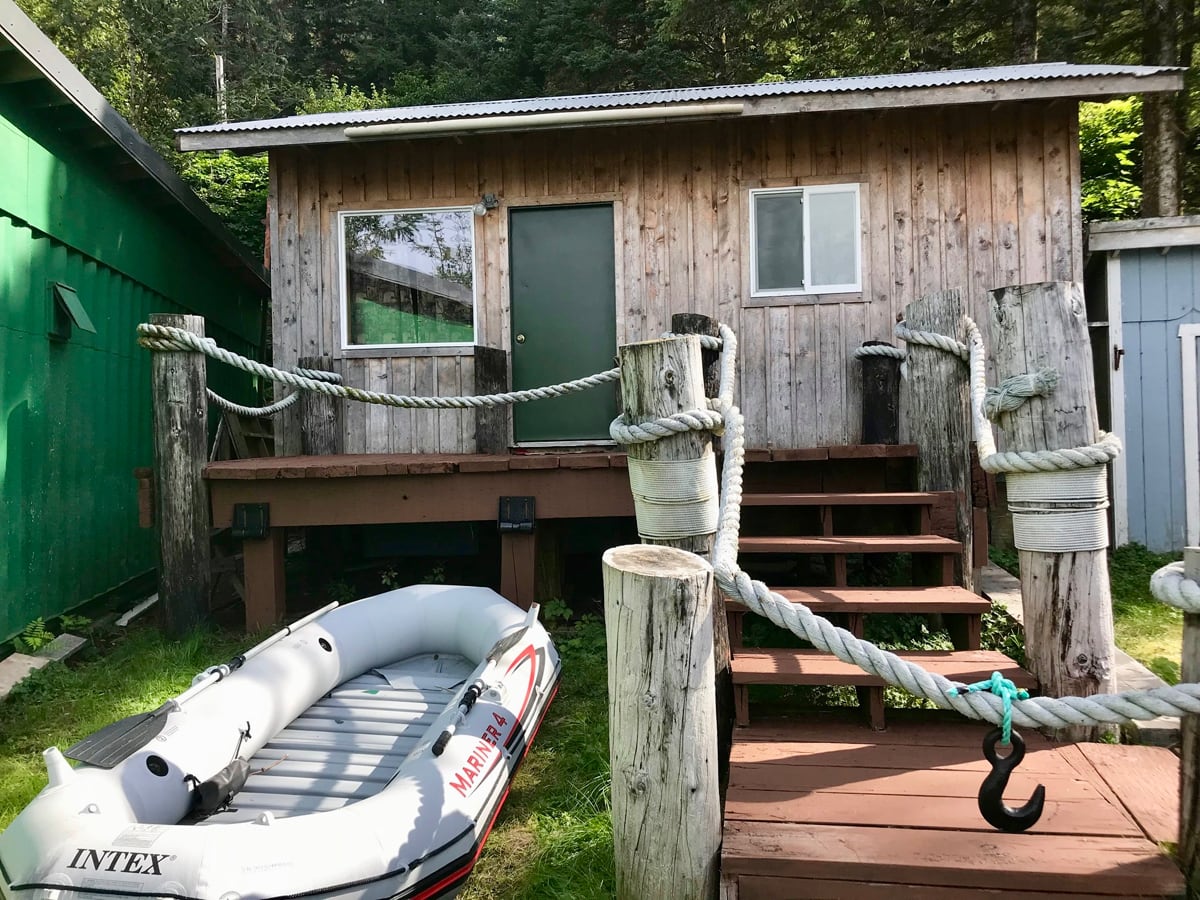 View of cabin with steps and patio with dinghy in the front yard.