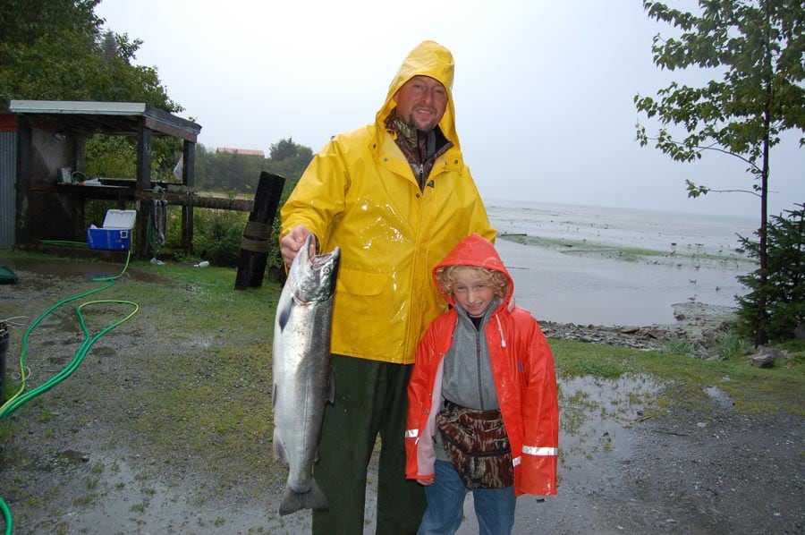 son with father holding fish while wearing raincoats