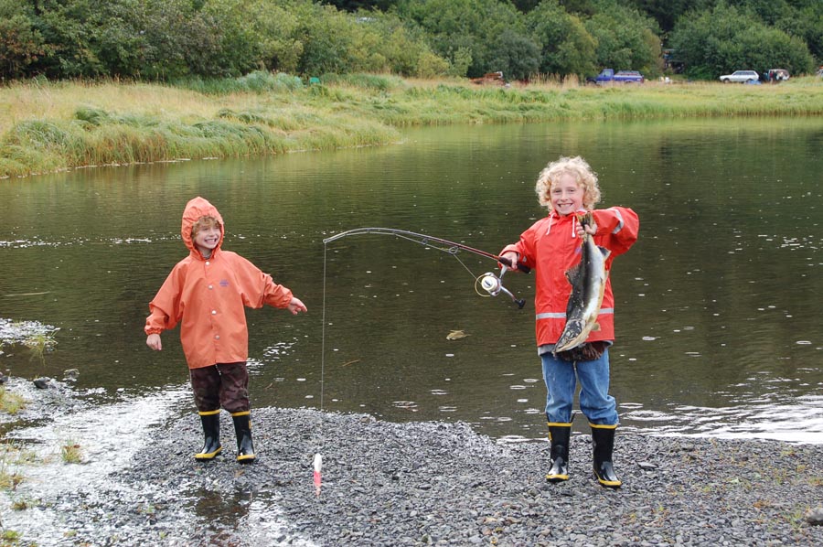 two boys next to inlet with one boy holding a rod and caught salmon