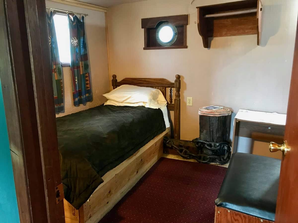 Bedroom with single bed, desk, an end table, and a porthole.